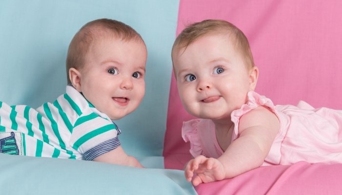 Adorable twin brother and sister lying in front of a pink and blue background.