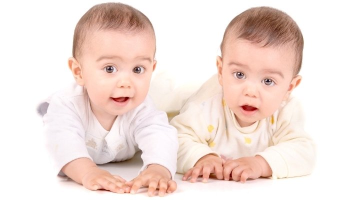 Two cute twin brothers on their tummies against a white background.