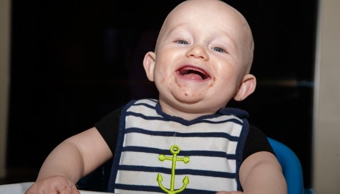 A cute baby boy with just one tooth sitting in his high chair wearing a sailor bib.