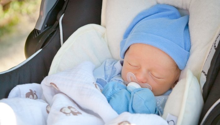 A tiny baby asleep in his stroller while wearing a blanket, a hat, and mittens.