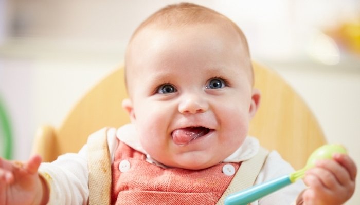A cute baby smiling with his tongue to one side while sitting in his high chair.