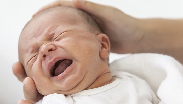 Close-up look at a screaming newborn being held by his father.