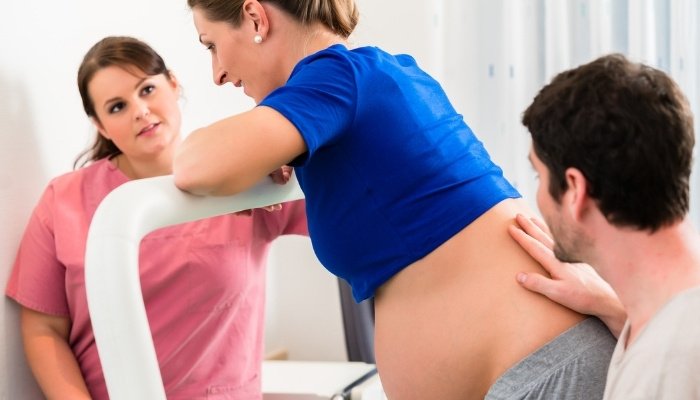A woman leaning on the hospital bed while standing to relieve discomfort during labor.