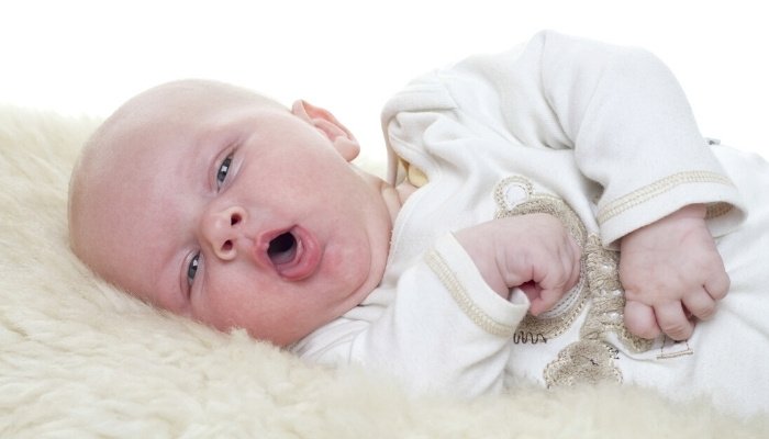 A little baby lying on his side while coughing.