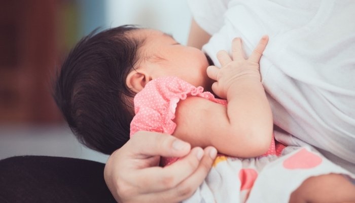 Close-up of baby girl in dress nursing from her mother.
