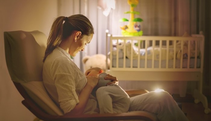 A young mother breastfeeding her baby at night in a dimly lit nursery.
