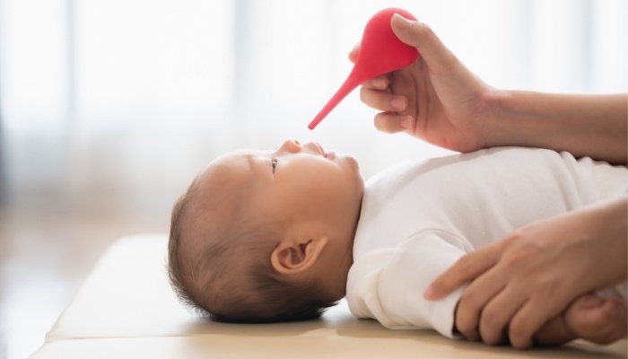 A mother preparing to use a bulb syringe to remove mucus from her baby's nose.