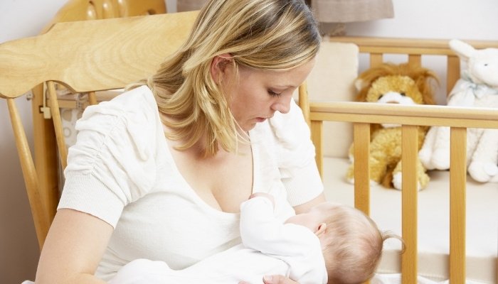 A mother sitting in a rocking chair in a nursery breastfeeding her baby.