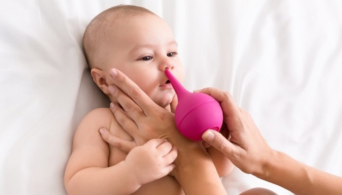 A mother using a bulb syringe to suction her baby's nose.