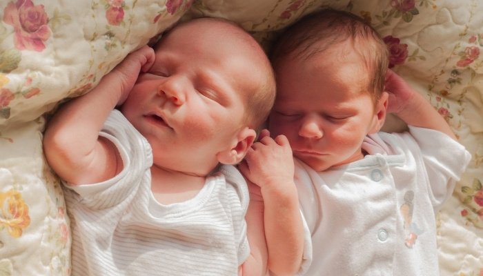 Newborn fraternal twins sleeping side by side while wearing onesies.