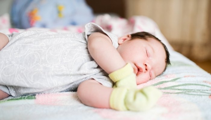 A newborn sleeping on his side while wearing a pair of yellow mittens.