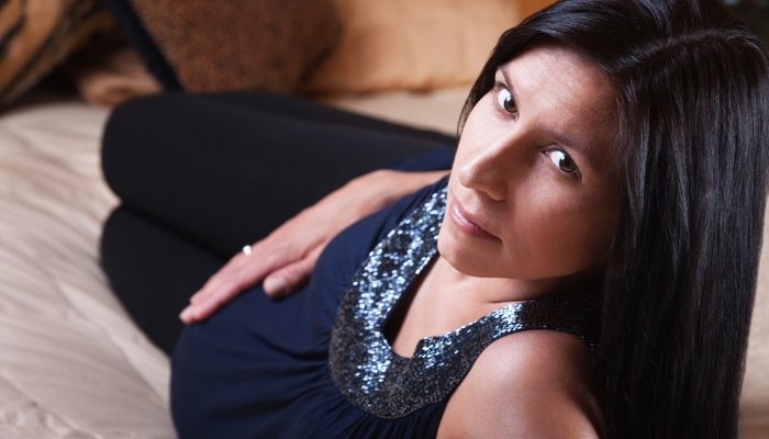 A pregnant lady lying in bed on her side looking over her shoulder.