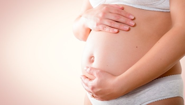 A pregnant lady in her underwear gently holding her baby bump.