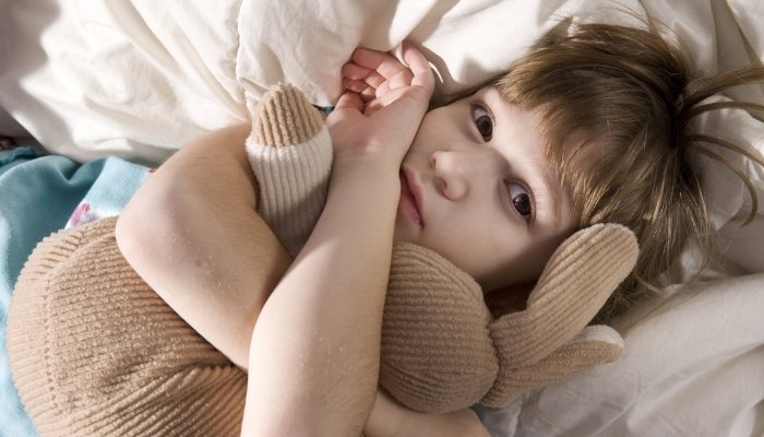 A sick little boy lying in bed holding on to a stuffed bunny rabbit.