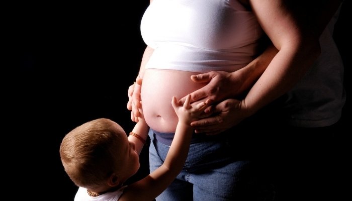 A toddler boy gently touching his mother's pregnant belly.