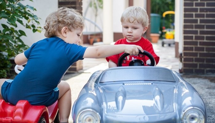 Two toddler boys riding their toy cars outside.