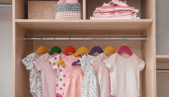 Baby clothes for a little girl hanging neatly on colorful hangers in a closet.