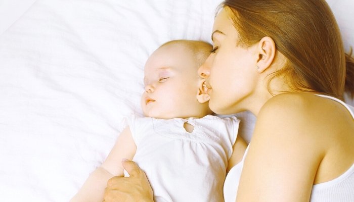 A young mother sleeping in bed with her baby cuddled up close.