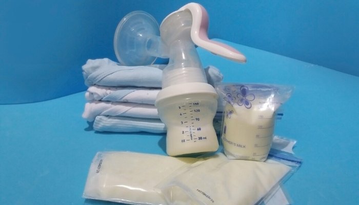 A manual breast pump beside bags of breast milk for storing on a blue background.