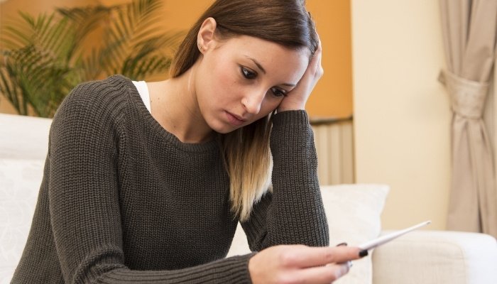 A disappointed woman staring at a pregnancy test while sitting on a couch.