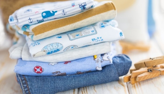A stack of freshly laundered and folded baby clothes and several clothespins.
