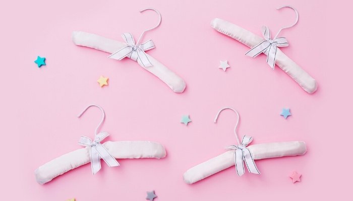 Four pink baby clothes hangers with bows on a pink background with decorative stars.