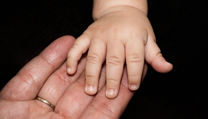 A baby's hand resting on her grandmother's outstretched hand on a black background.