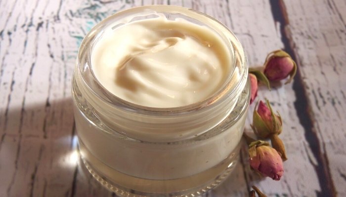 Homemade body lotion in a glass jar with flower buds resting beside it.