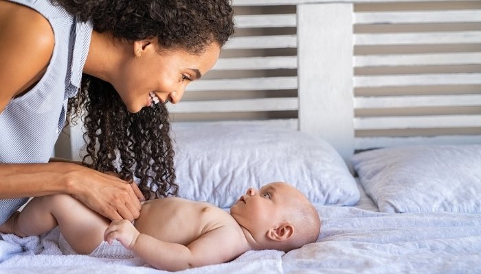 A young mother just finishing putting a clean diaper on her baby boy.