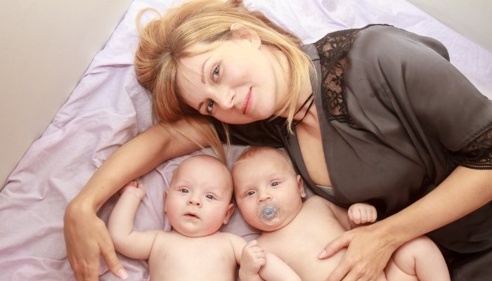 A new mother lies in bed snuggling with her twin babies.