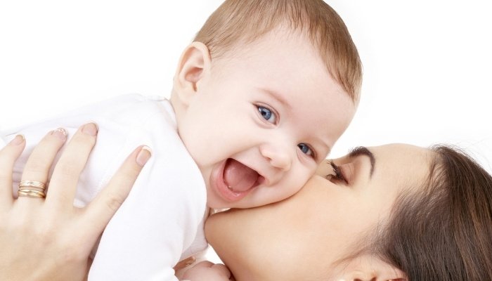 A mother gives her happy baby a kiss on the cheek.