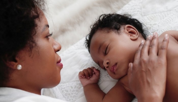 A young mother keeps her hand on her baby's chest while watching him sleep.