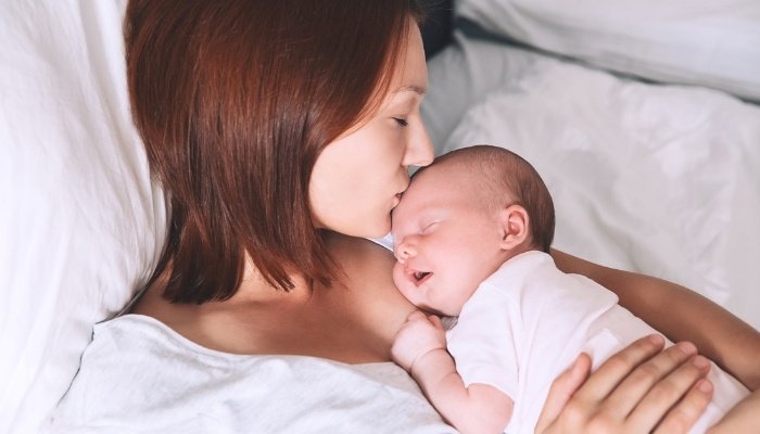 A mother holding her newborn against her chest while resting in bed.