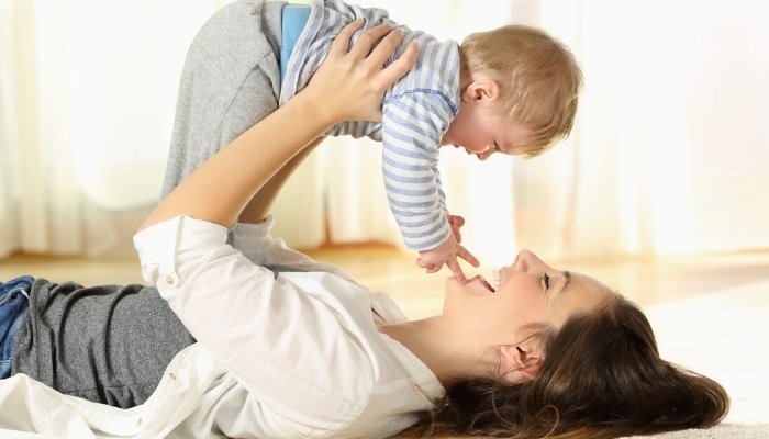 A mother lying on her back holding her little boy in the air above her.