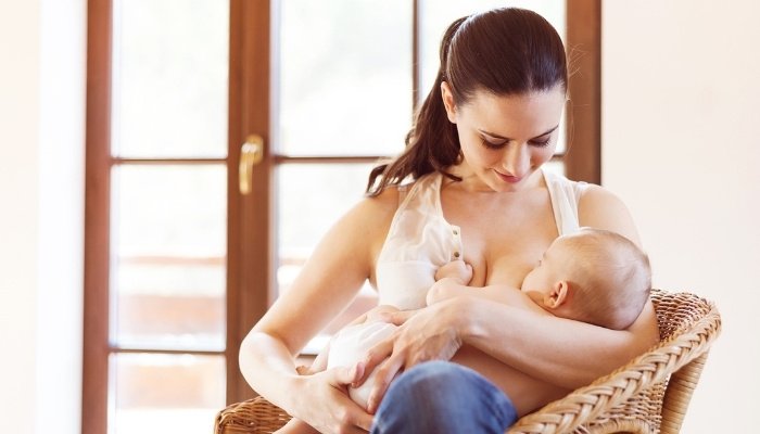 A young mother nursing her baby near a bright doorway.