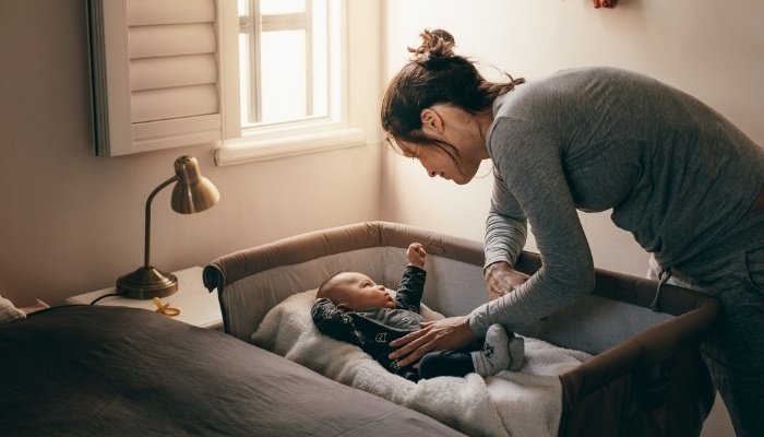 A young mother bending over the bassinet trying to wake her baby.