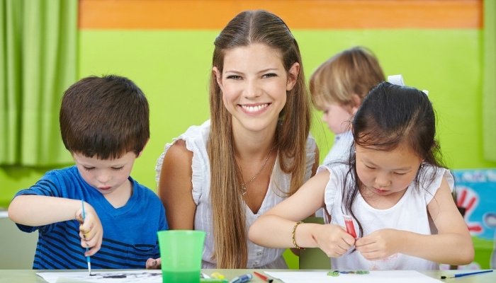 A nanny watching several children paint pictures.