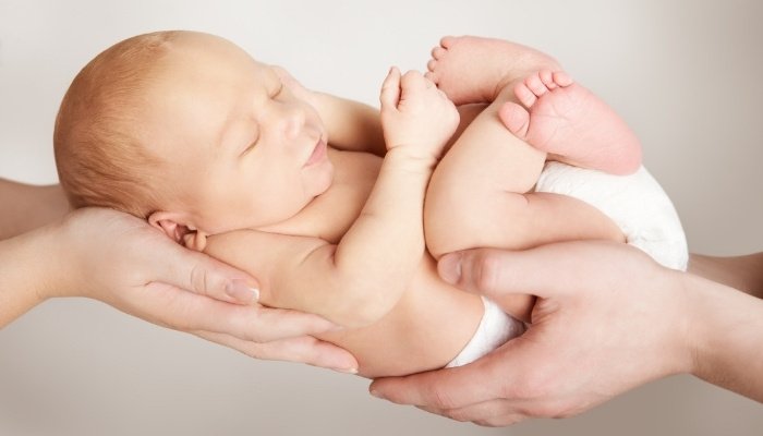 Hands of mother and father holding a new baby in the air.