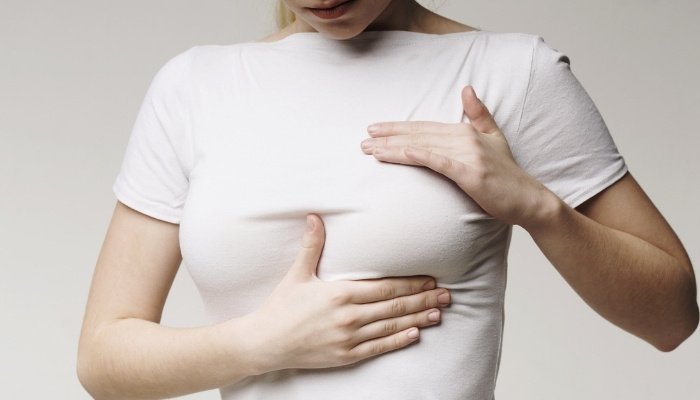 A woman taking stock of her breasts through her white shirt.