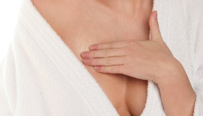 A woman in a white bathrobe massaging her breast.