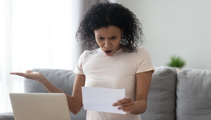 A young woman shocked and angry at the bill in her hand.