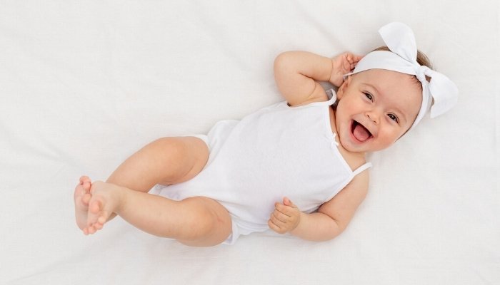 A happy, smiling baby girl lies awake in a white crib.