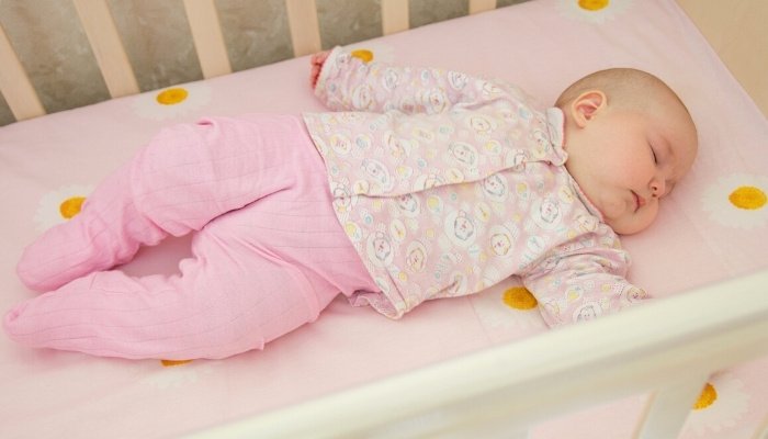 A cute baby girl sleeping on her back in a white crib.