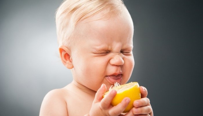 A baby making a funny face after tasting a lemon.