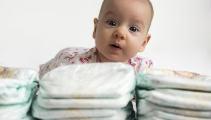 A baby on her tummy peering over piles of diapers.