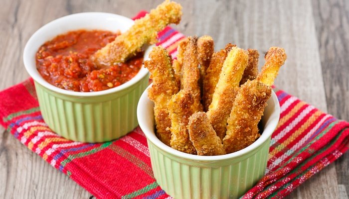A cup of zucchini fries and a sauce for dipping on a colorful towel.