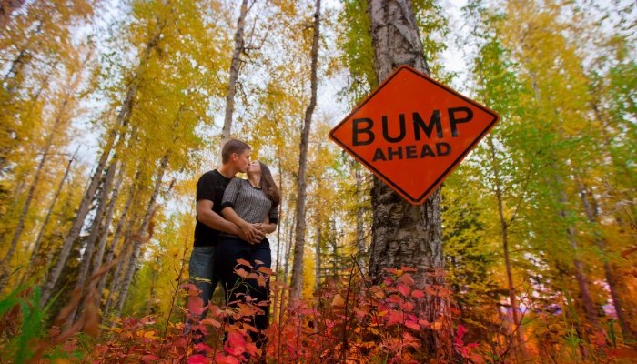 A couple kissing beside a Bump Ahead sign.