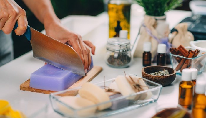 A lady uses a large knife to cut a lavender block of homemade soap.