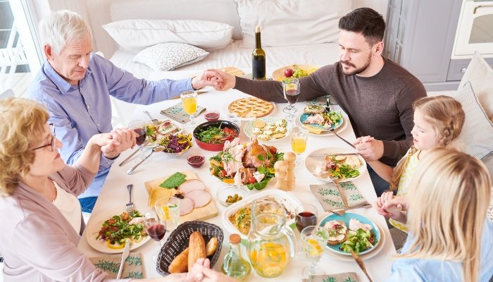 Parents, children, and grandparents praying together before enjoying a meal.