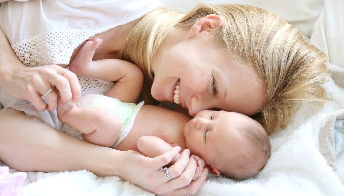 A blonde mother snuggling with her newborn baby.
